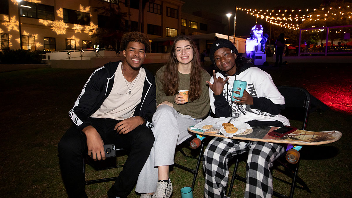 Three students sitting in lawn chairs on Sunken Garden with cups of cocoa