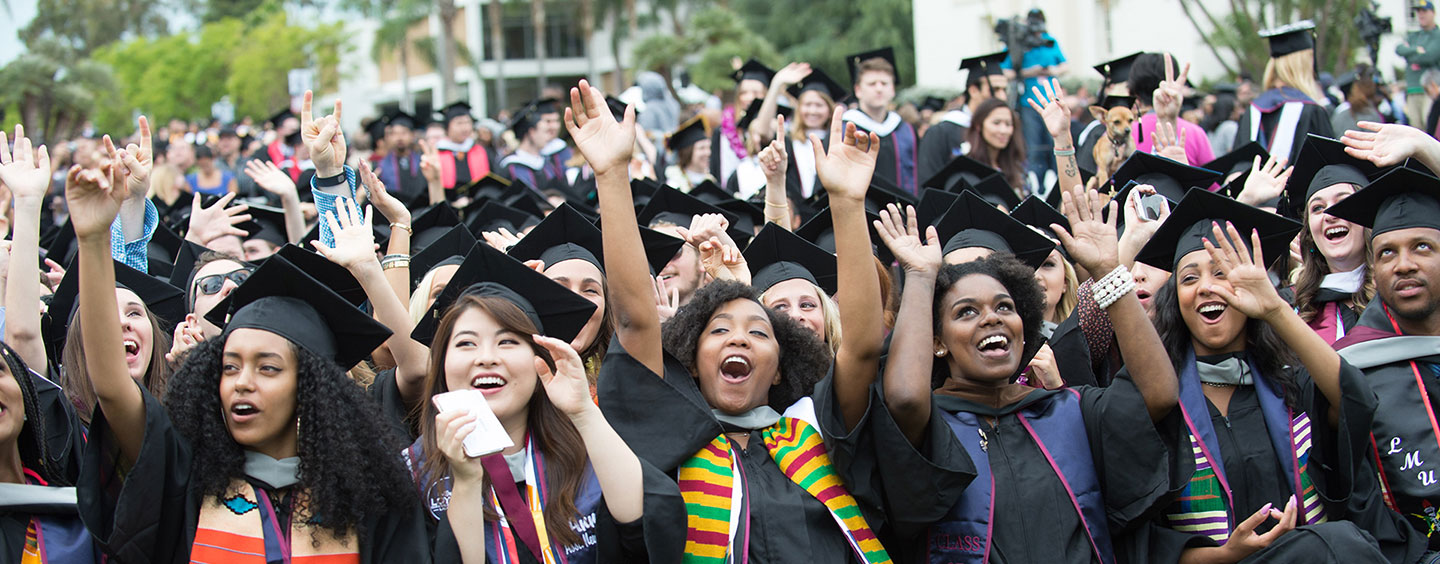 Graduates raising their hands and cheering from their seats during commencement