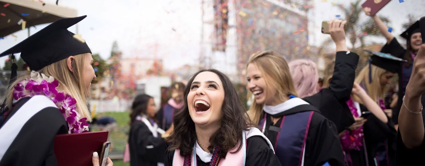 Students cheering and celebrating after the completion of commencement as confetti falls around them